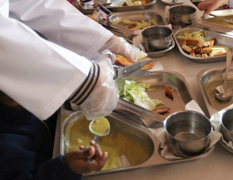 Trabajadora comedor escolar cortando el filete a un niño 