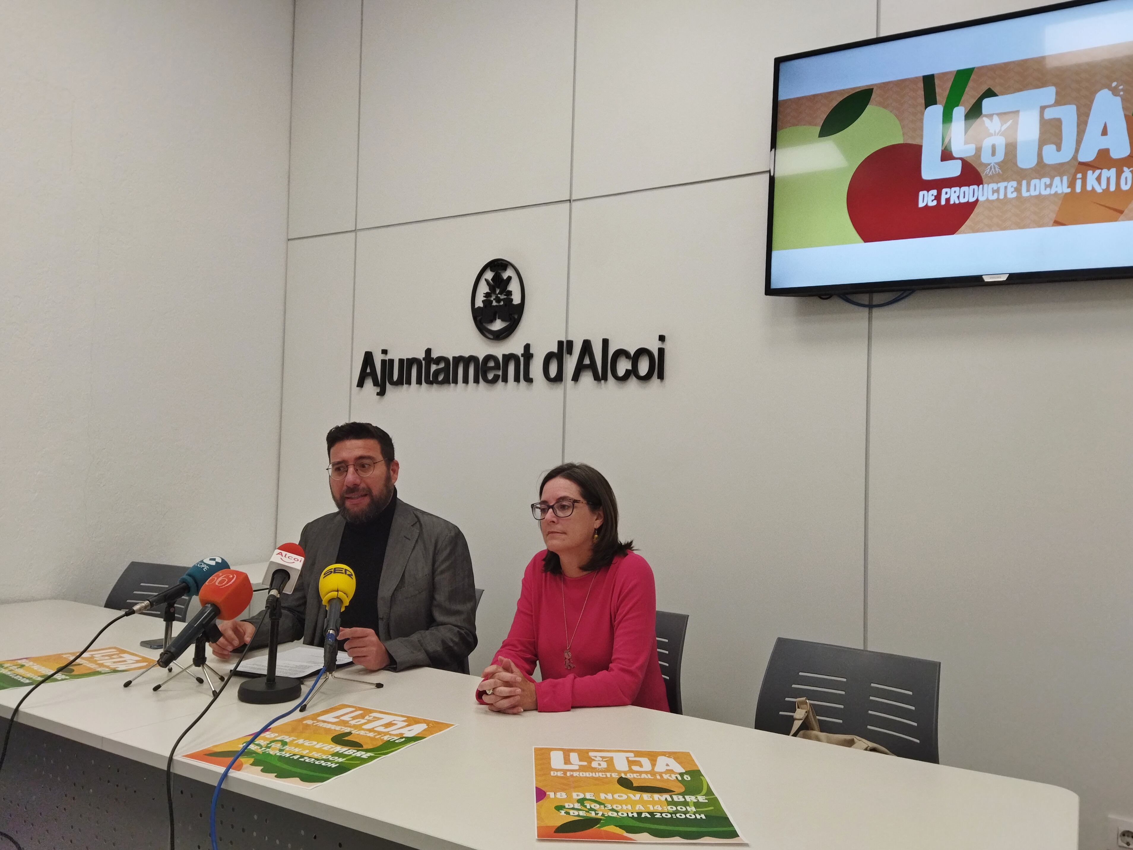 Àlex Cerradelo, vicealcalde y edil de Comercio, e Inma Sancho, ADL de la Mancomunitat de l'Alcoià i el Comtat presentando la I Llotja de Producte Local i Km. 0.