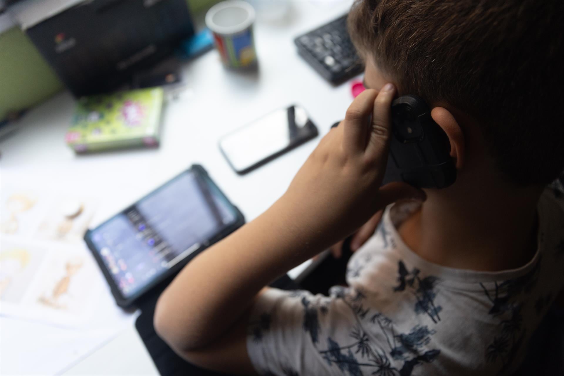 Un niño usa el teléfono móvil y una tablet.