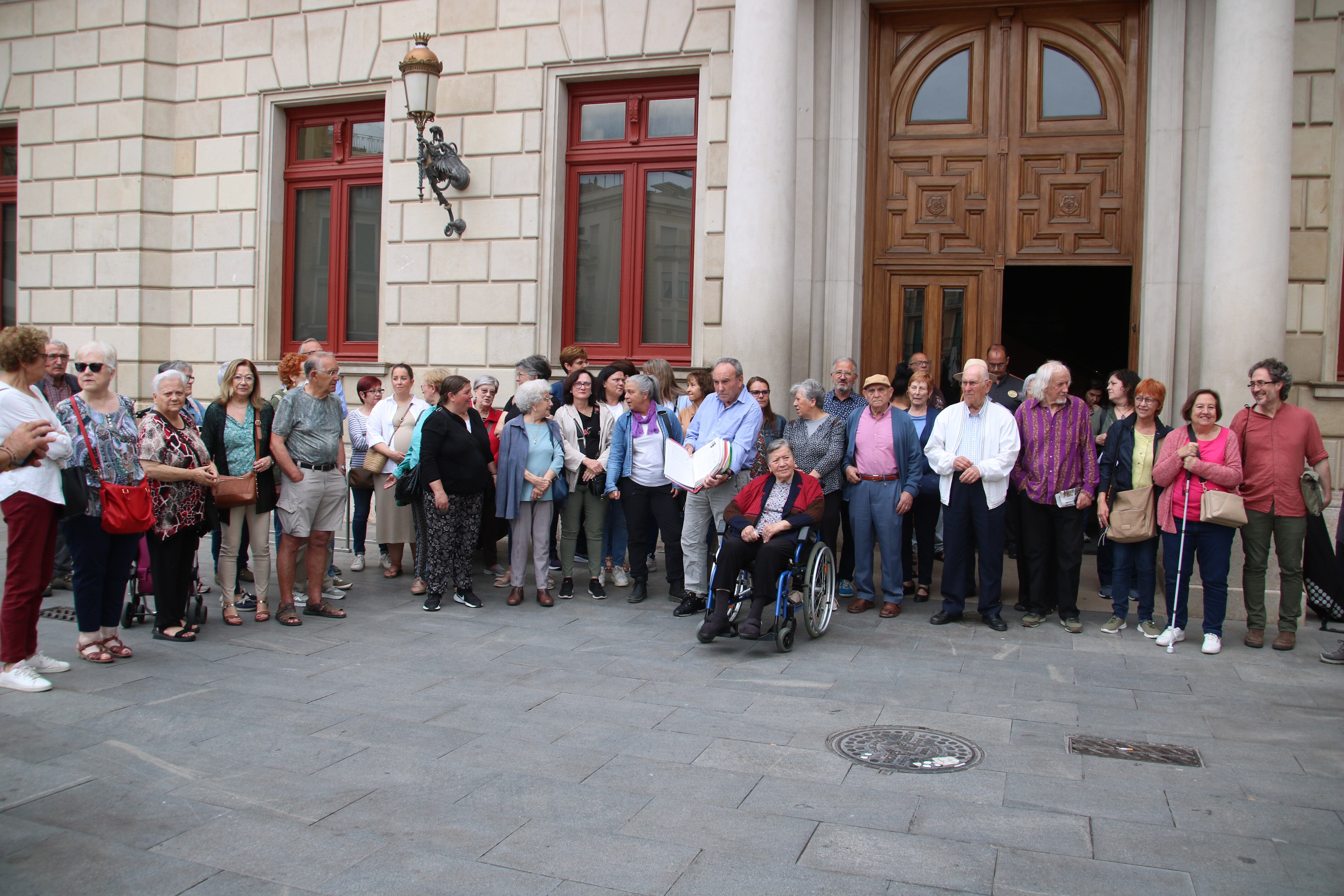 Familiars, usuaris i treballadors de la residència de Reus davant de l&#039;Ajuntament minuts abans d&#039;entregar les firmes recollides per aturar el trasllat dels residents a altres centres