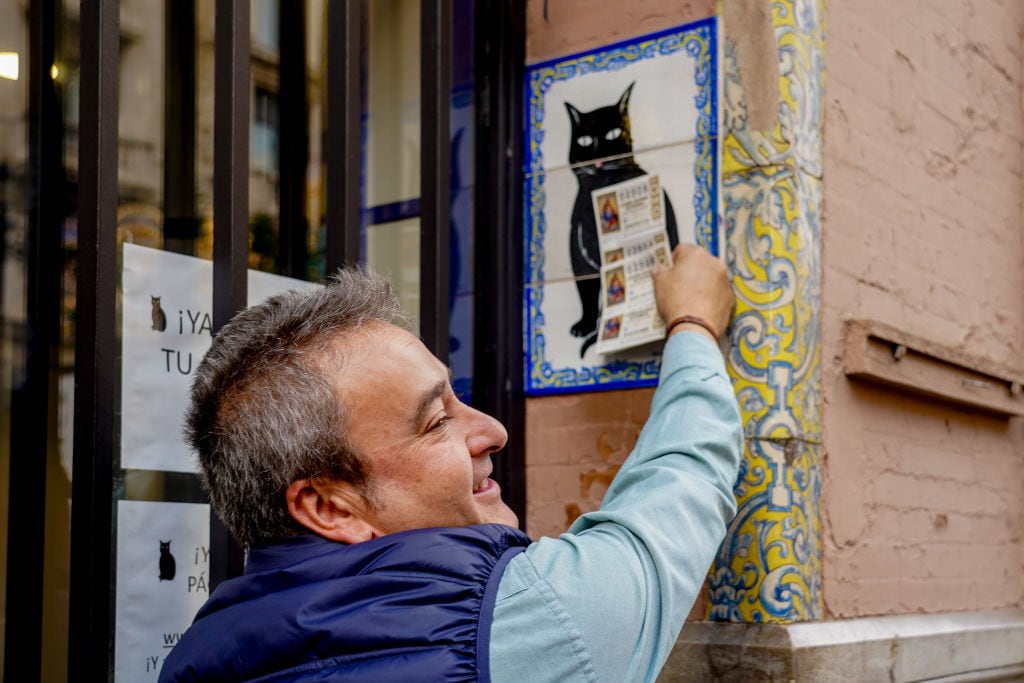 Un jugador de la Lotería de Navidad pasa su décimo por el logo de la administración &#039;El Gato Negro&#039;.