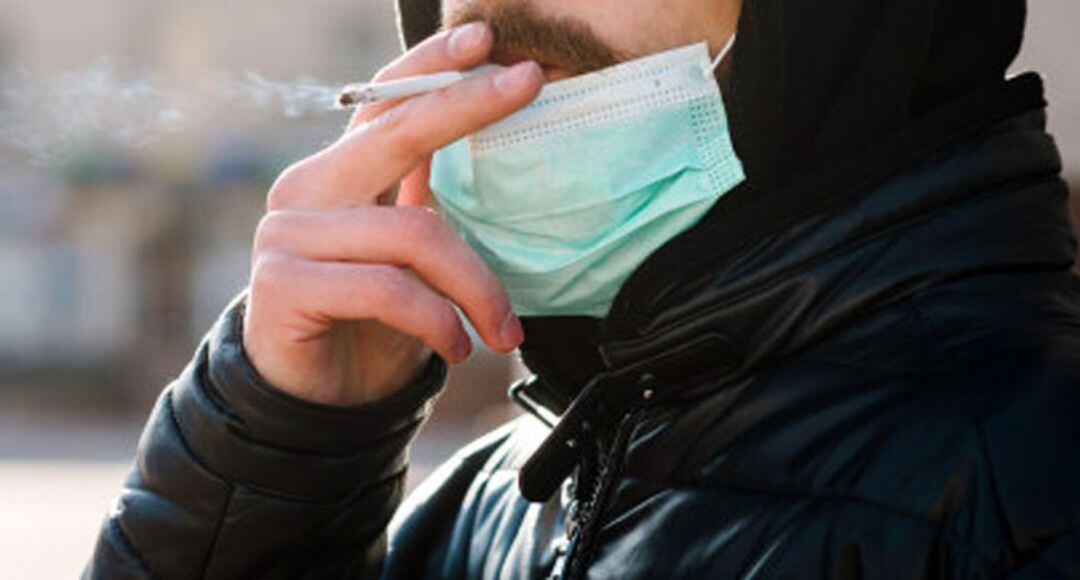 Un hombre con mascarilla fuma un cigarro.