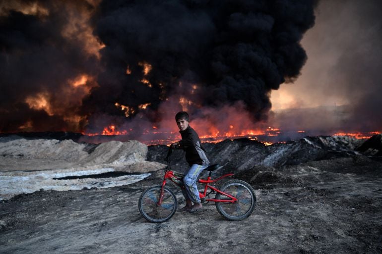 Un niño toma un descanso mientras pasa por un campo de petroleo que fue quemado por Daesh