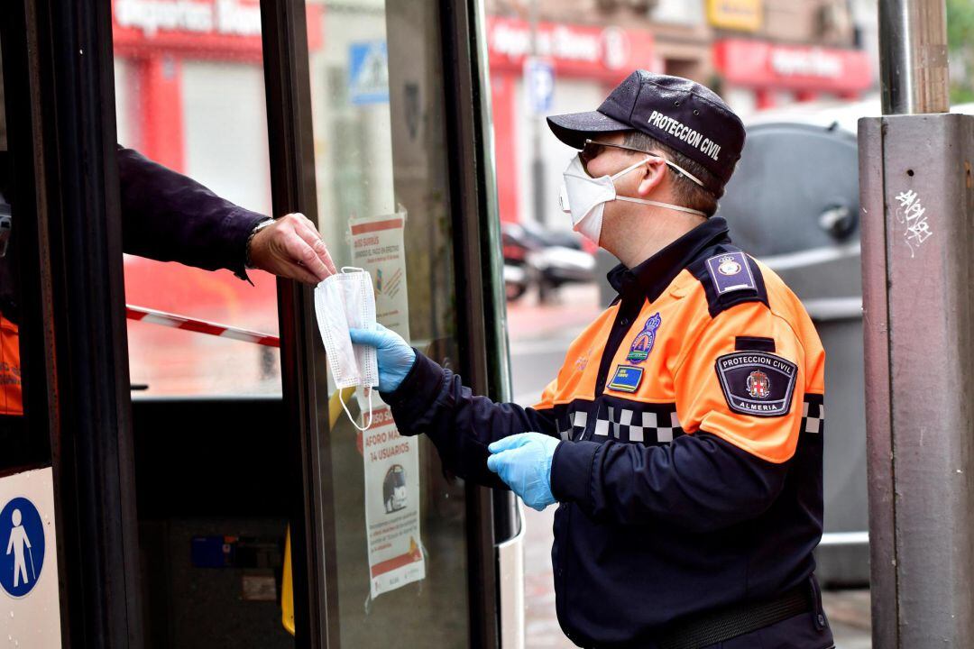 Un miembro de Protección Civil entrega una mascarilla a una persona montada ya en un autobús