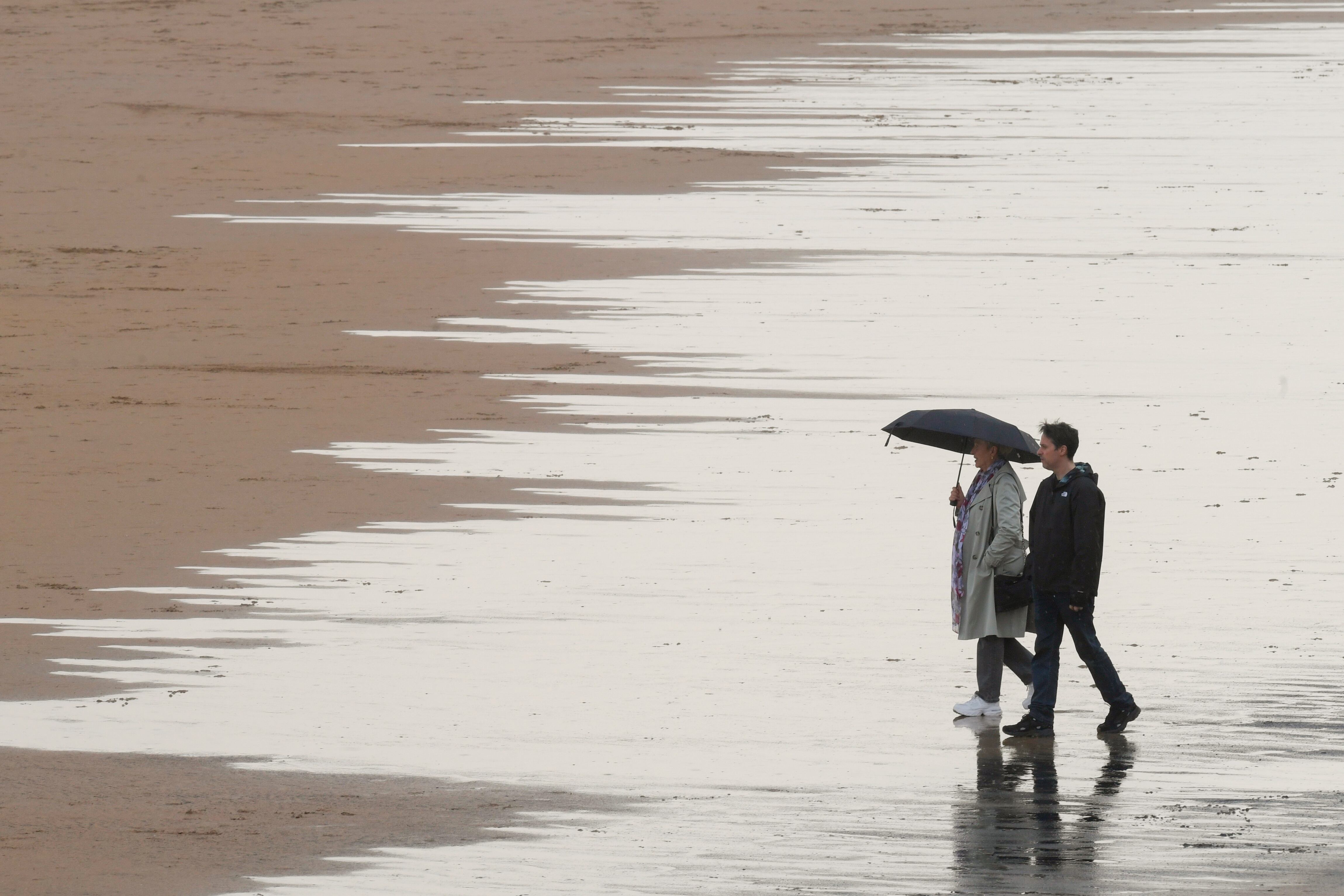 Gente paseando bajo la lluvia en la Playa de San Lorenzo de Gijon.