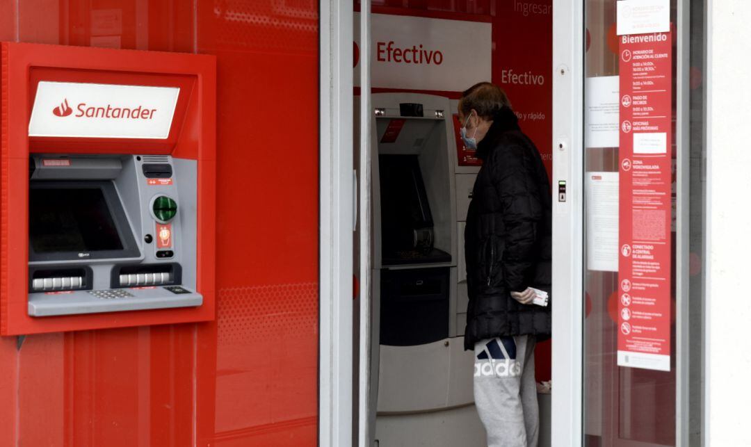 Un hombre saca dinero de un cajero del Banco Santander.