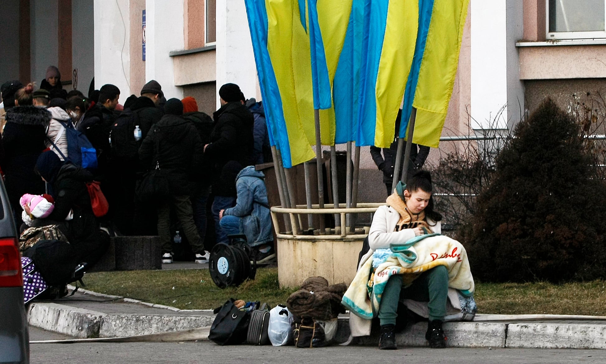 Una madre amamanta a su bebé junto a varias banderas ucranianas mientras aguarda en la frontera, junto con otros cientos de refugiados ucranianos, poder entrar en Polonia, este jueves en la localidad ucraniana de Hlynytsi