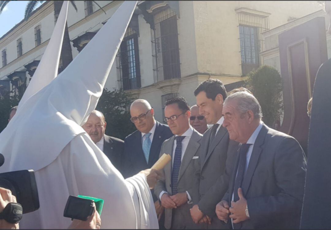 El presidente de la Junta de Andalucía, Juanma Moreno, junto al presidente de la Unión de Hermandades recibiendo a un nazareno de la Hermandad de la Sed