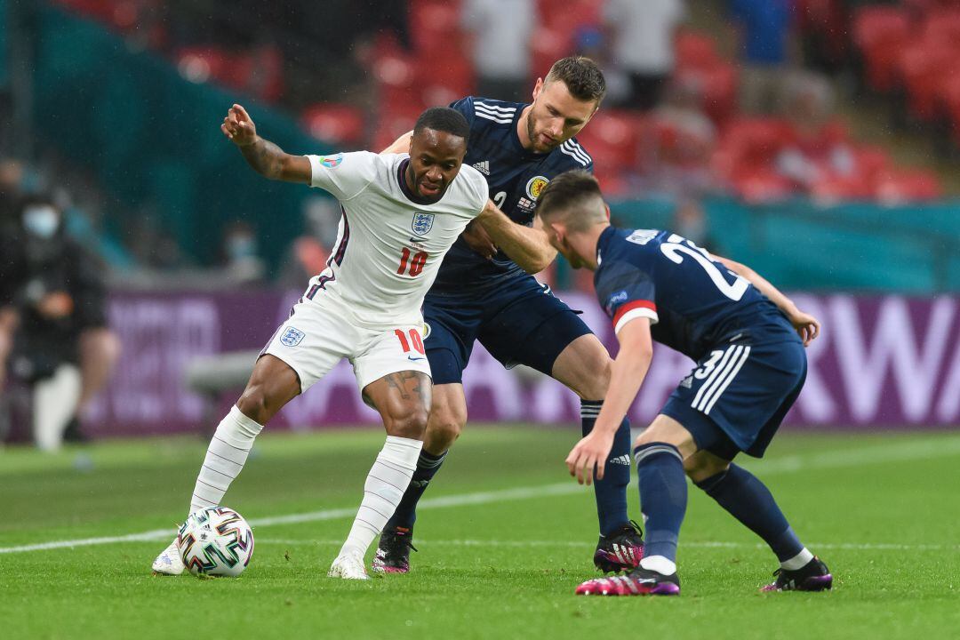 Sterling protege el balón frente a dos defensas escoceses