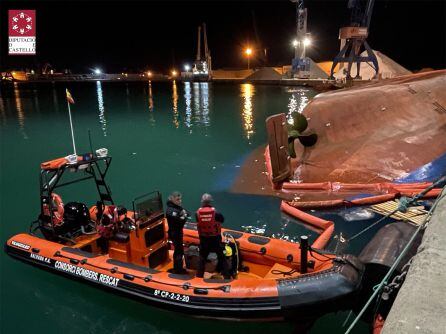 Imagen de Emergencias trabajando en la búsqueda de dos personas. Al lado, el buque volcado