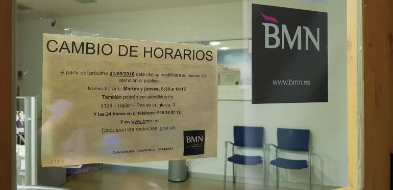 Las oficinas de BMN en localidades pequeñas, como esta de Válor (Granada), comenzaron en 2017 a reducir su horario de atención al público, como muestra el cartel