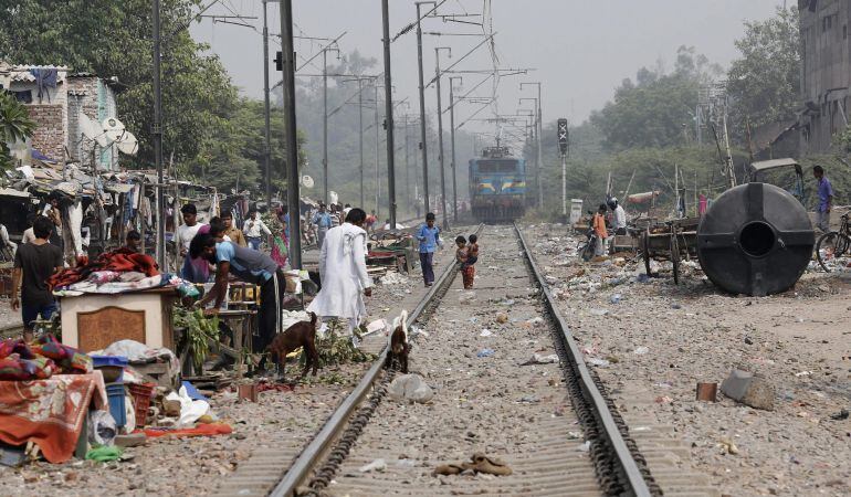 Varias personas caminan por las vías de un tren en un barrio de chabolas donde una niña de cuatro años fue violada en Nueva Delhi (India).