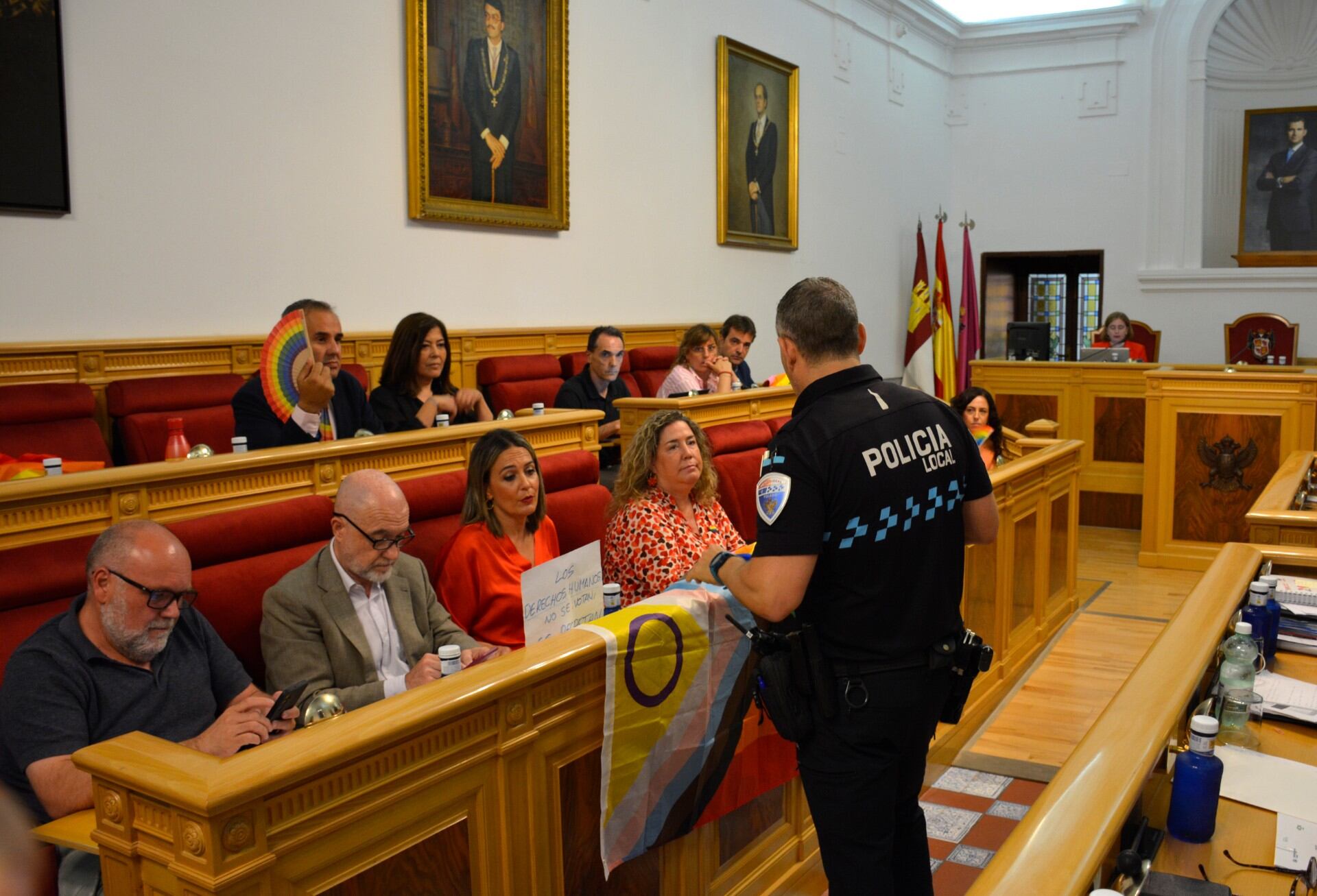 Un policía local se acerca a la bancada del PSOE para retirar la bandera arcoíris durante el Pleno celebrado este jueves en Toledo