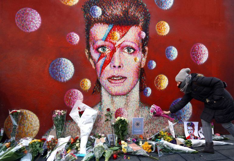 A woman leaves flowers beneath a mural of David Bowie in Brixton on January 11, 2016 in London, England. British music and fashion icon David Bowie died earlier today at the age of 69 after a battle with cancer. 