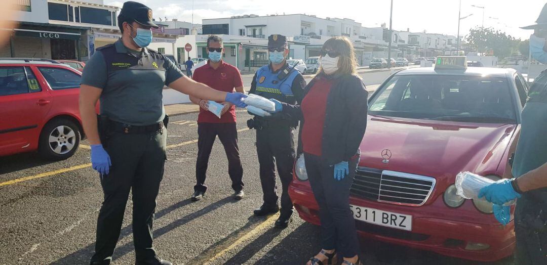 Un agente del puesto de la Guardia Civil de Yaiza repartiendo mascarillas a usuarios de taxis en Playa Blanca jujno a un agente de la Policía Local.