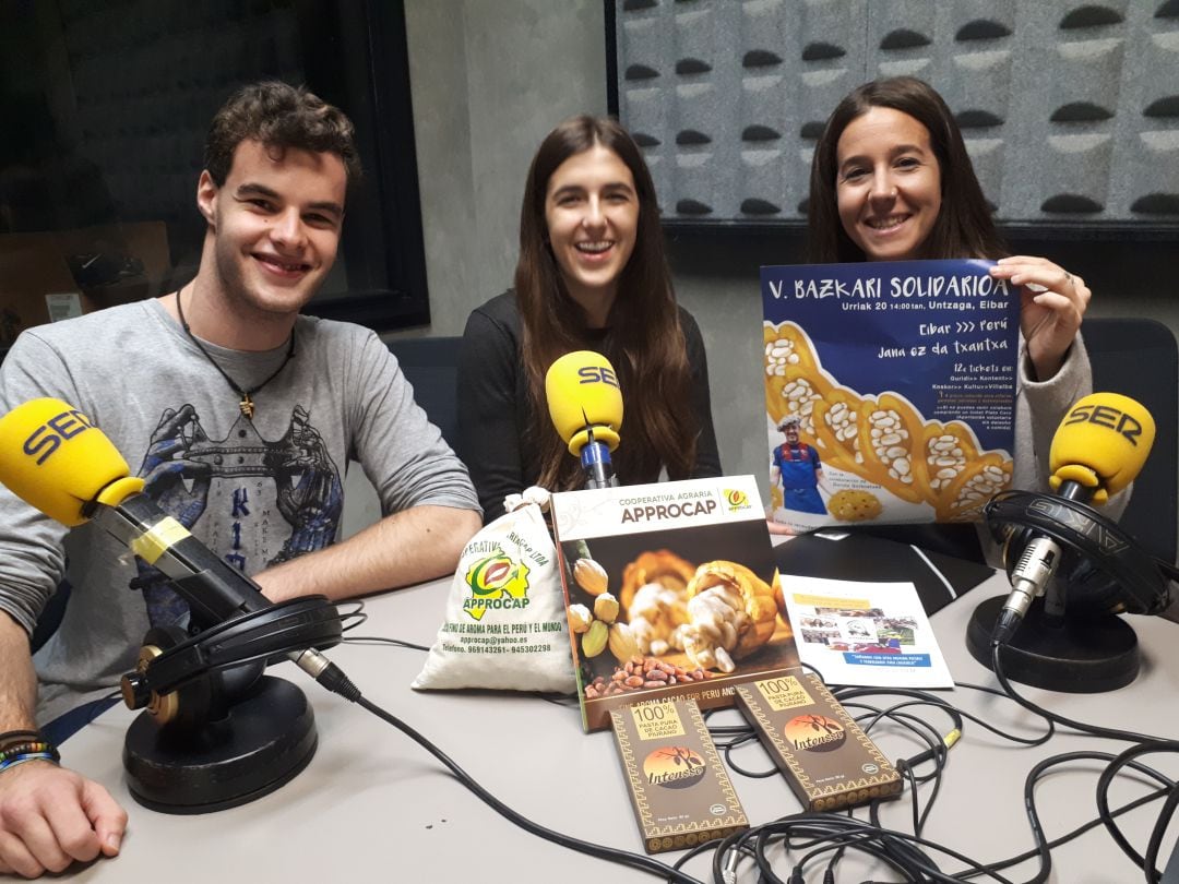 Iker Urbieta, Ainhoa bilbatua y Alaia Berrioxabal posan con el cartel anunciador de la comida y productos de comercio justo