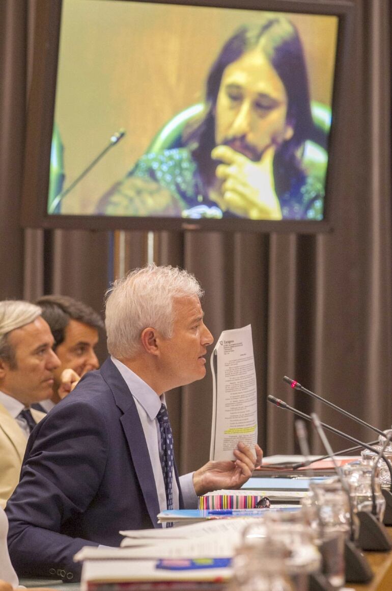 El portavoz del PP, Eloy Suárez (abajo), se dirige al concejal de Zaragoza en Común, Pablo Híjar (en la pantalla), durante el debate de la moción. 