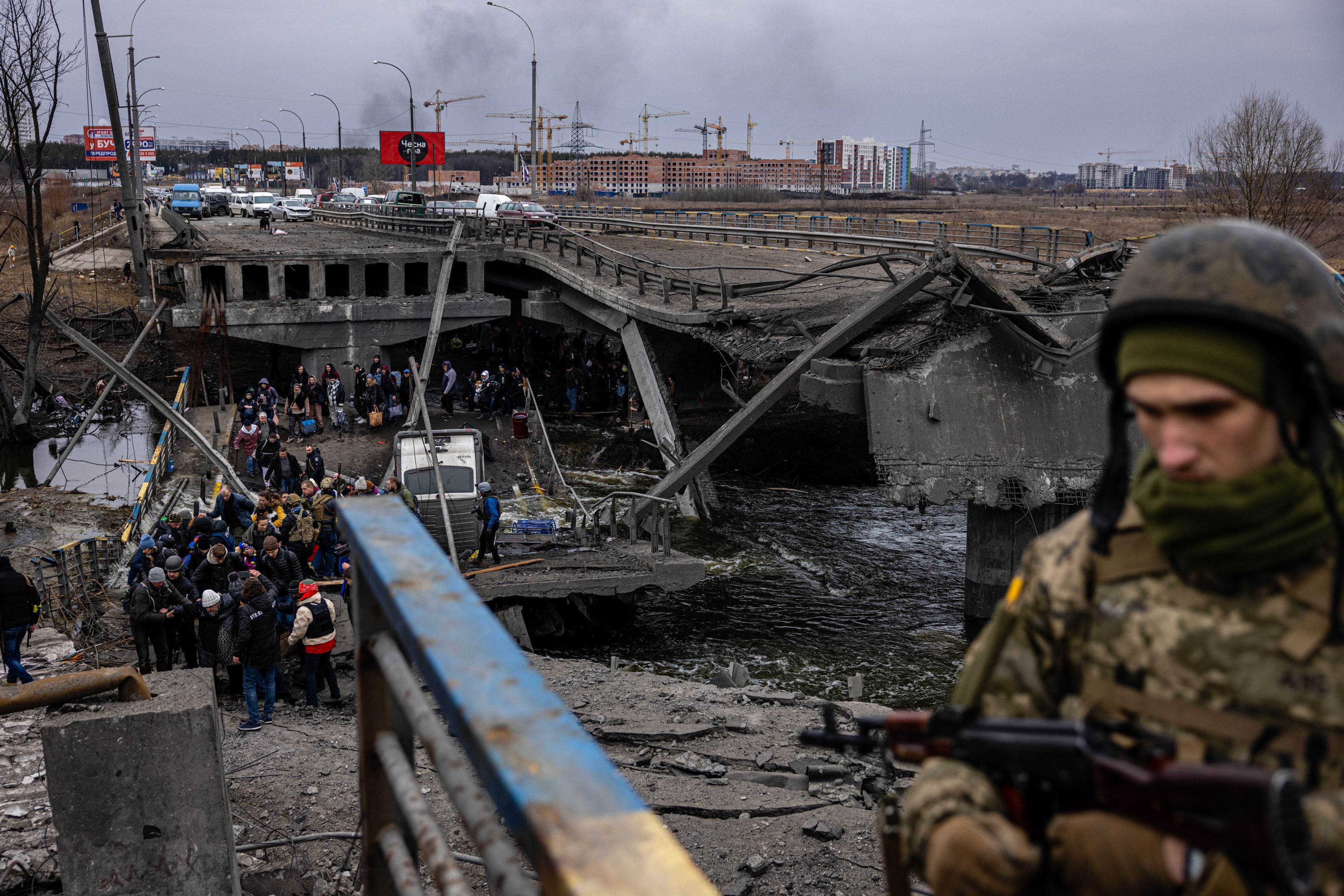 Un soldado ucraniano junto a cientos de civiles que atraviesan un puente destruido en Kiev