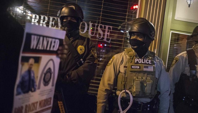 Los manifestantes sostienen pancartas del oficial Darren Wilson y pasan junto a los policías que custodian un negocio en Ferguson, Missouri