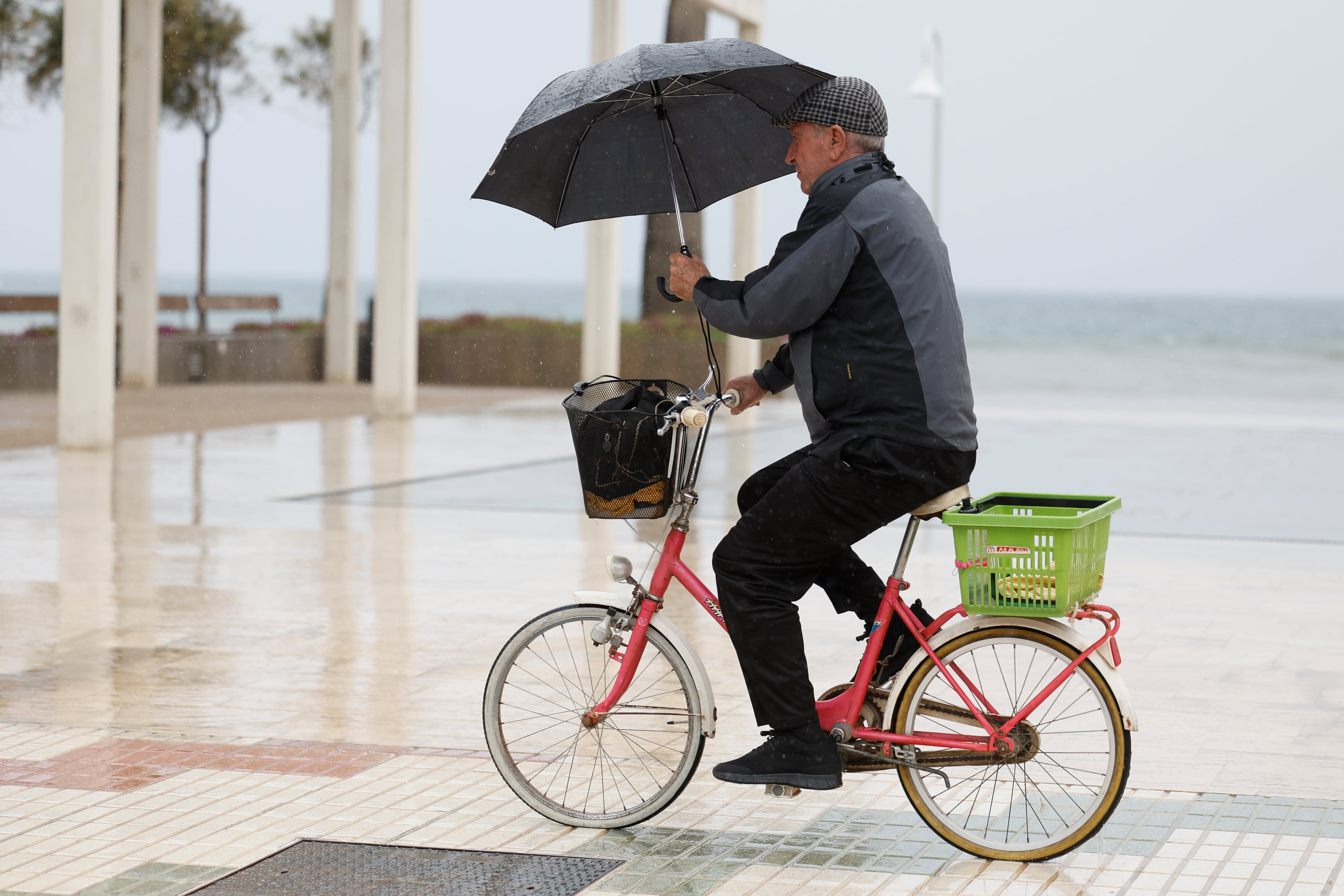 GRAFAND6633. RINCÓN DE LA VICTORIA (MÁLAGA), 28/02/2025.- Un hombre pasea en bicicleta resguardándose de la lluvia con un paraguas en el Rincón de la Victoria (Málaga), este viernes con alertas de lluvia y tormentas en Andalucía. EFE/Jorge Zapata
