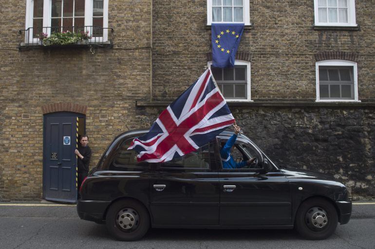 Un taxista londinense ondea una bandera británica mientras circula por una calle donde una bandera europea ondea en una ventana en Londres