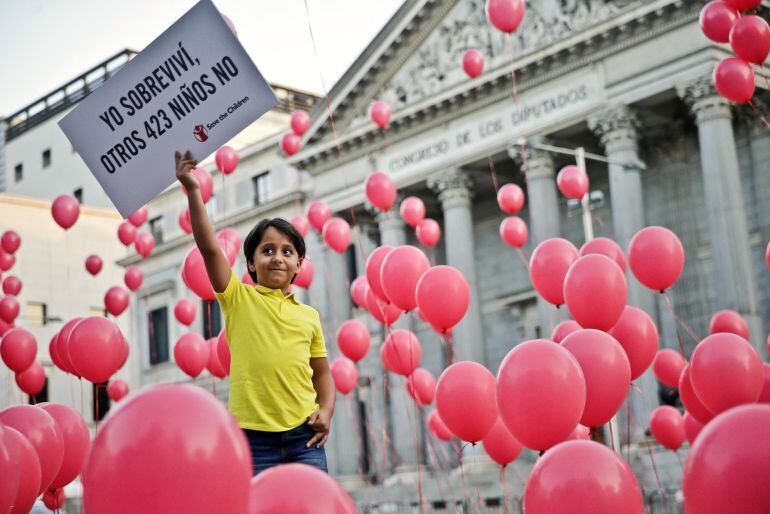 Said, un niño sirio de 8 años, que vive desde hace un año junto a su hermano Mohammed, de 17, y el padre de ambos, Osama Abdul Mohsen, en Getafe (Madrid), muestra un cartel durante el acto organizado por Save the Children a las puertas del Congreso de los