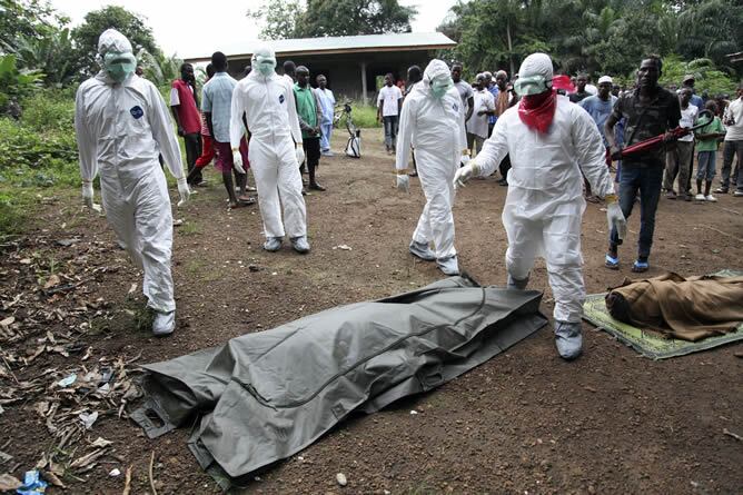 Enfermeros liberianos a punto de trasladar los cuerpos de dos víctimas del ébola para su entierro en la comunidad de Banjor, a las afueras de Monrovia (Liberia)