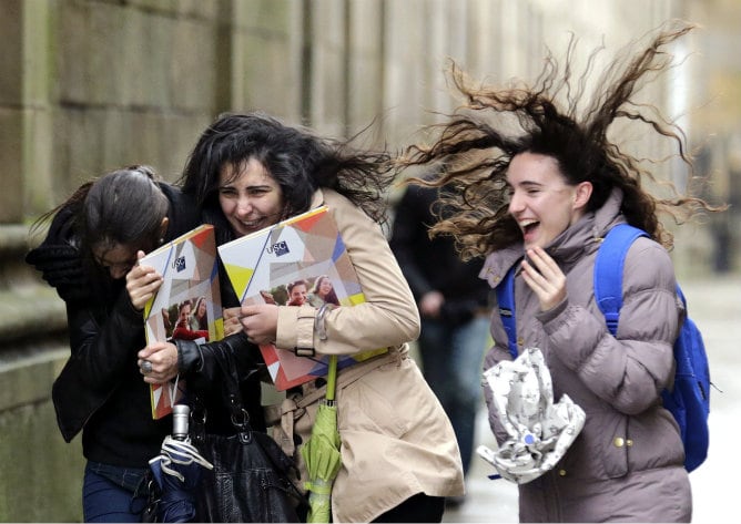 Un grupo de estudiantes a su paso por la plaza del Obradoiro se protege del fuerte viento registrado en Santiago de Compostela