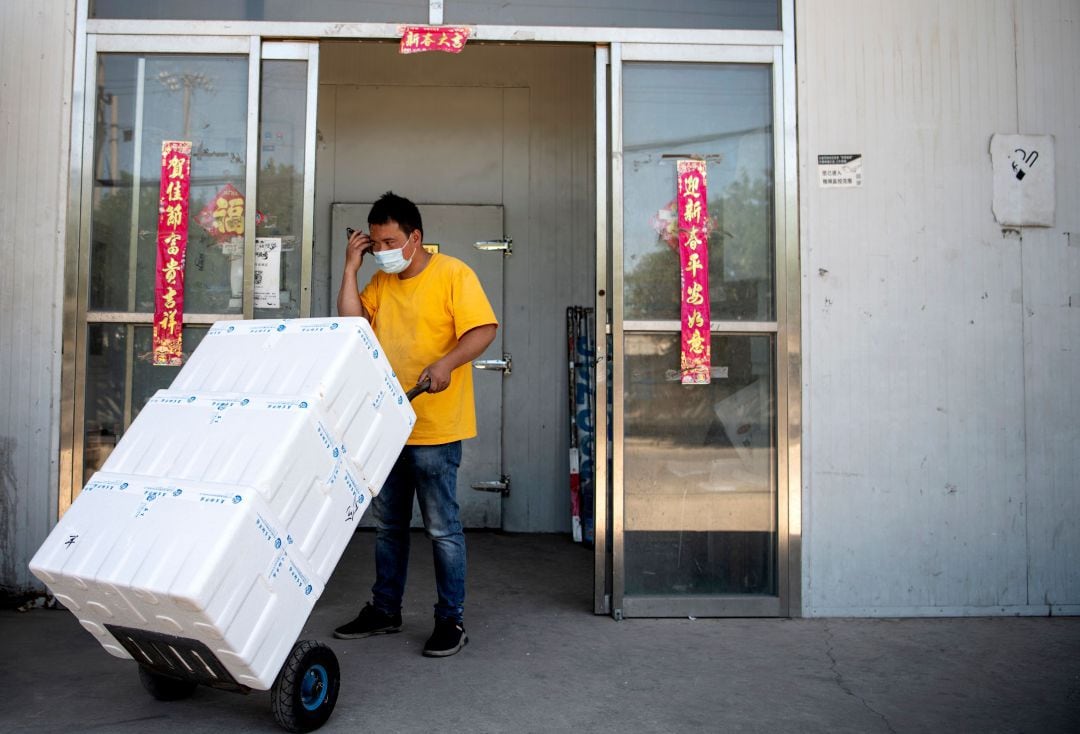 Un trabajador habla por teléfono móvil mientras transporta cajas en el mercado cerrado de Xinfadi en Pekín