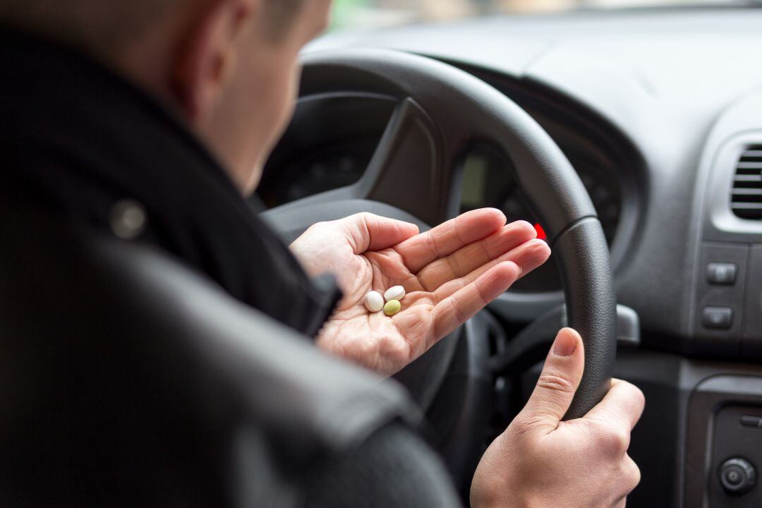 Un hombre ingiere varias pastillas mientras conduce.