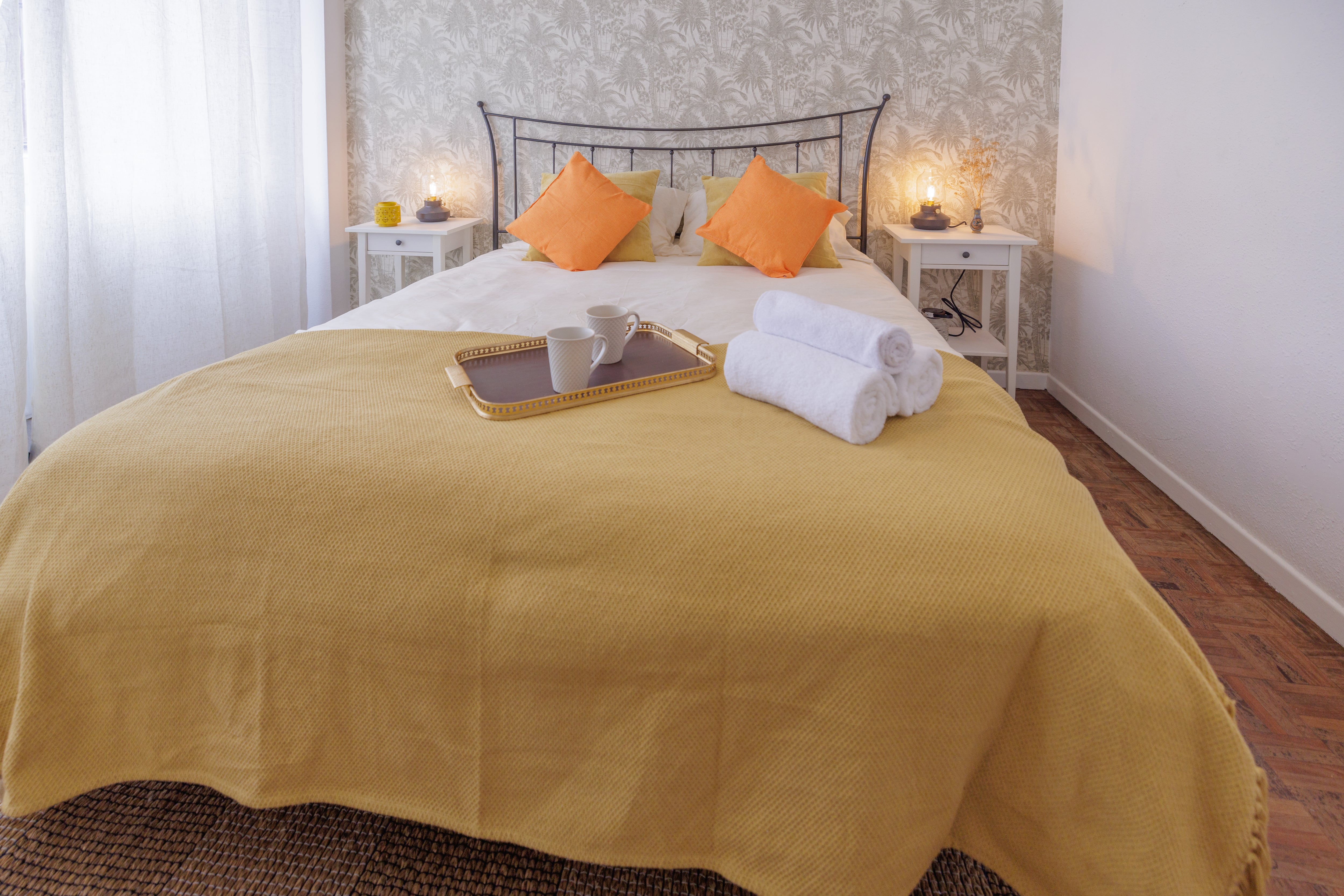 This inviting bedroom features a plush bed with a soft yellow blanket and bright orange pillows. A golden tray with coffee cups and fresh towels adds a touch of luxury. Soft lighting and floral wallpaper create a soothing ambiance, while natural light streams through sheer curtains, enhancing the room&#039;s warm and welcoming atmosphere.
Bilbao, Biscay, Spain - July 13, 2024