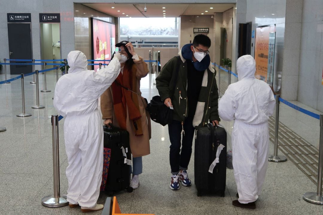 Los trabajadores en trajes de protección controlan la temperatura de los pasajeros que llegan a la estación Xianning North, una ciudad que limita con Wuhan