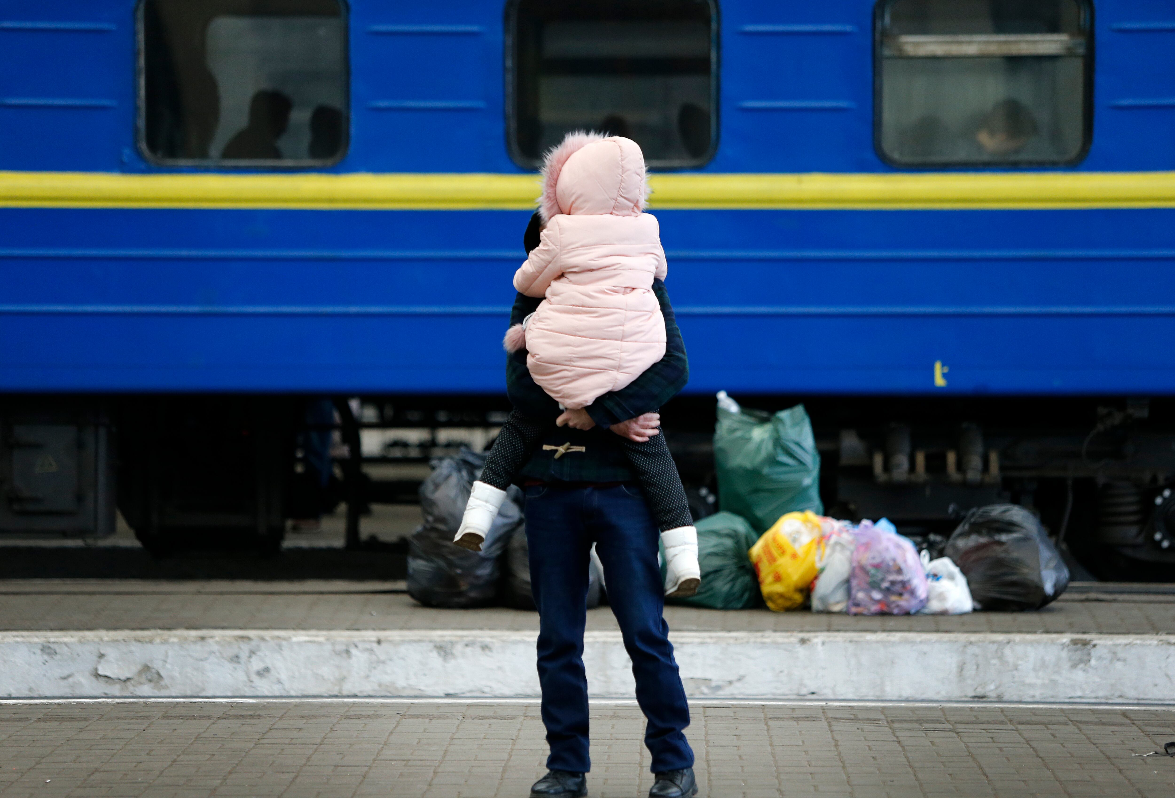 L&#039;VIV (UCRANIA), 02/03/2022.- Un padre con su hija en brazos en la estación de trenes de L&#039;Viv (Ucrania) esperando para huir hacia Polonia como consecuencia de los bombardeos rusos en la ciudad de Kiev. Al fondo, se observa un tren lleno de pasajeros. EFE/Manuel Lorenzo
