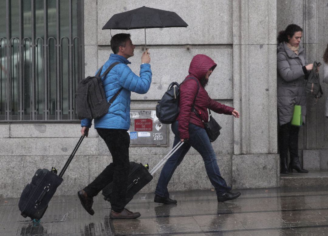 Dos turistas se refugian de la lluvia con paraguas, en Madrid (archivo).