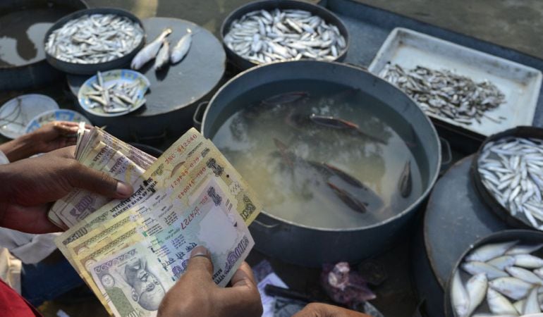 Un vendedor indio cuenta varios billetes de 100 y 500 rupias en un mercado de pescado de la ciudad de Guwahati.