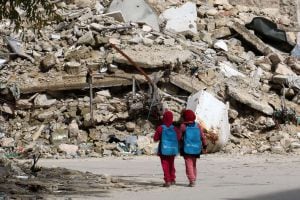 Syrian girls, carrying school bags provided by UNICEF, walk past the rubble of destroyed buildings on their way home from school on March 7, 2015 in al-Shaar neighbourhood, in the rebel-held side of the northern Syrian city of Aleppo. Heavy fighting shook