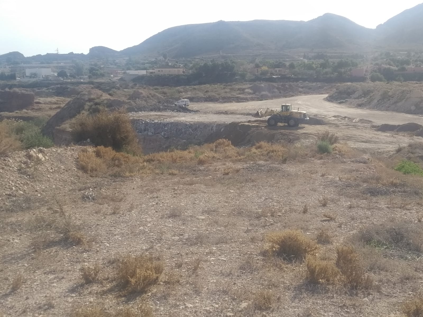 Una excavadora intentando enterrar los escombros en unos terrenos de Agost