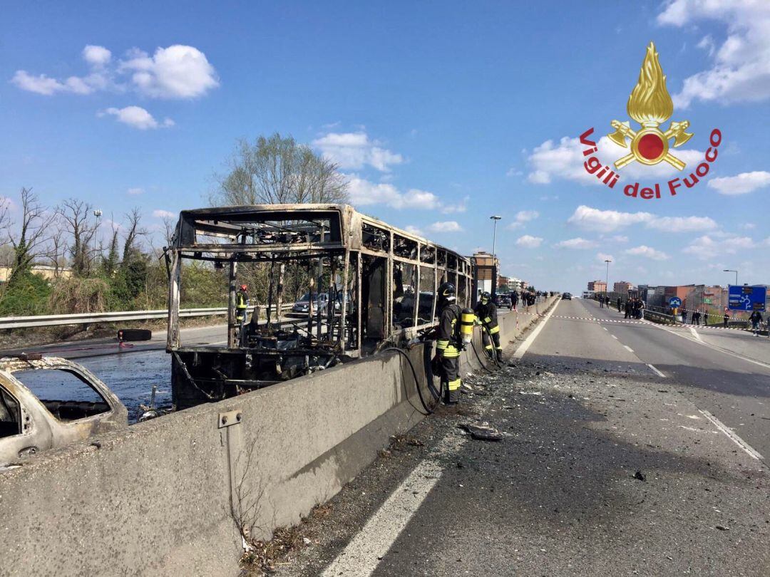 Los bomberos locales ante el autobús calcinado.