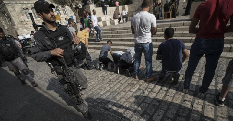 Un militar israelí patrulla mientras varios palestinos rezan fuera de la Puerta de los Leones, el acceso principal al complejo en el que se encuentra la Mezquita de Al Aqsa en Jerusalén (Israel). Siguen los enfrentamientos diarios entre palestinos y fuerz