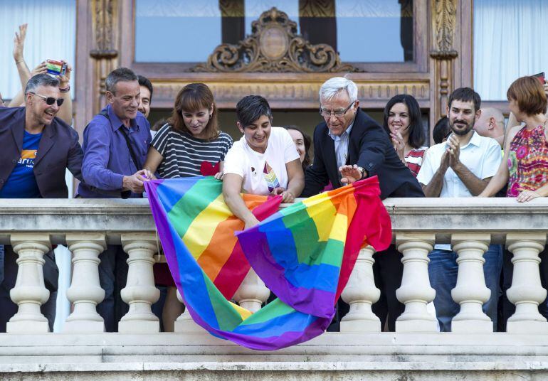 El alcalde de Valencia, Joan Ribó (centro), despliega, esta tarde, desde el balcón del Ayuntamiento la bandera arco iris con motivo del Día Internacional del Orgullo Lésbico, Gay, Transexual y Bisexual. En la imagen Ribó junto a Fany Boronat, coordinadora de Lambda (centro con camiseta blanca), y otros representantes del colectivo LGTB