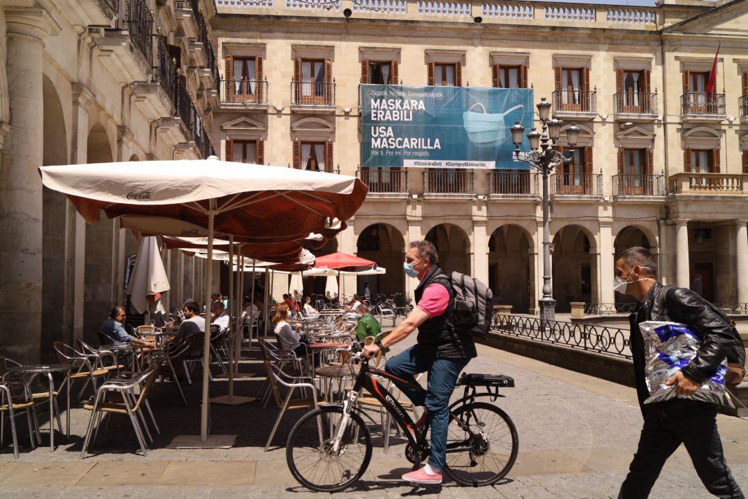 Un hombre con mascarilla pasea en bicicleta al lado de una terraza de una céntrica calle de Vitoria-Gasteiz