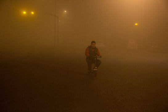 Un hombre fuma mietras monta en bici rodeado de polución en Pekín.