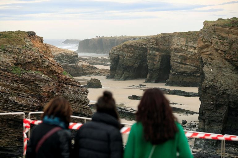 Varias personas observan la playa de As Catedrais en la que murió una joven. El arenal está cerrado al paso.