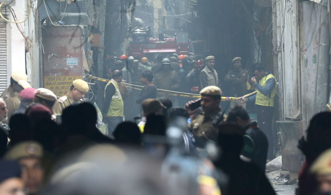 Policías indios, personal de defensa civil y bomberos se paran en un camino estrecho cerca del sitio donde estalló un incendio en Nueva Delhi