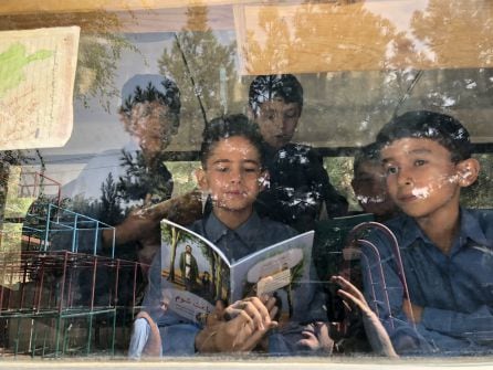 Unos niños leen libros al lado de los ventanales del autobús-biblioteca