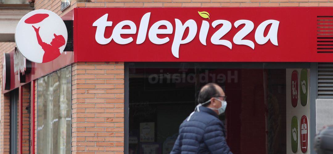 Un hombre protegido con mascarilla pasea cerca de un local de Telepizza 