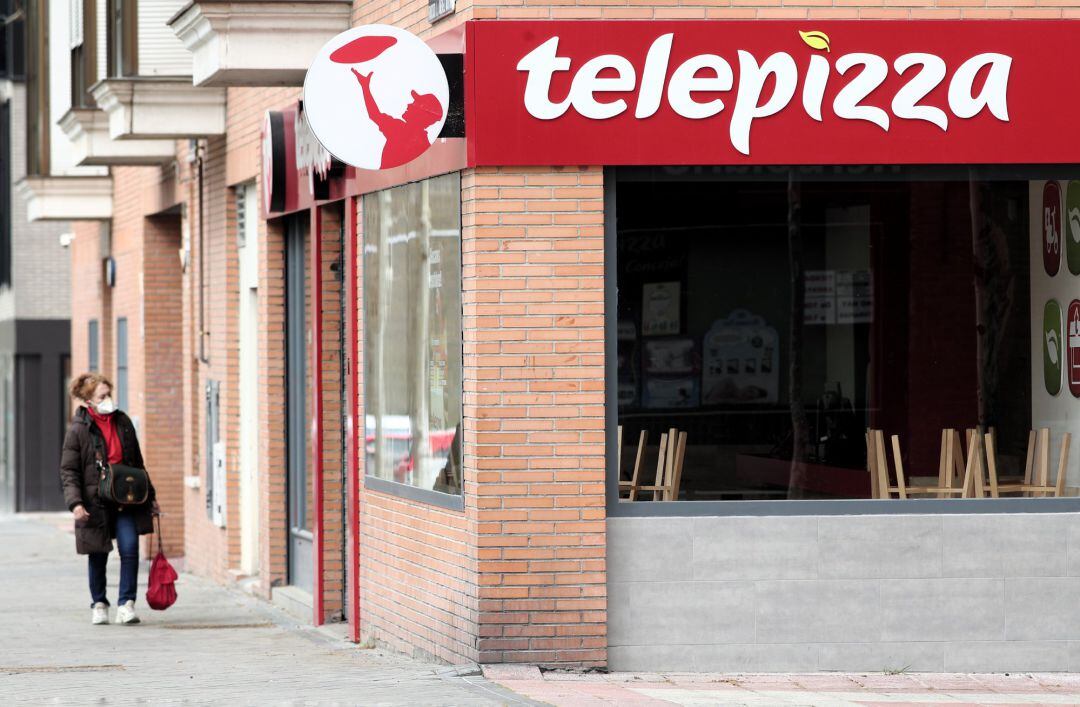 Una mujer protegida con mascarilla pasea cerca de un local de Telepizza 