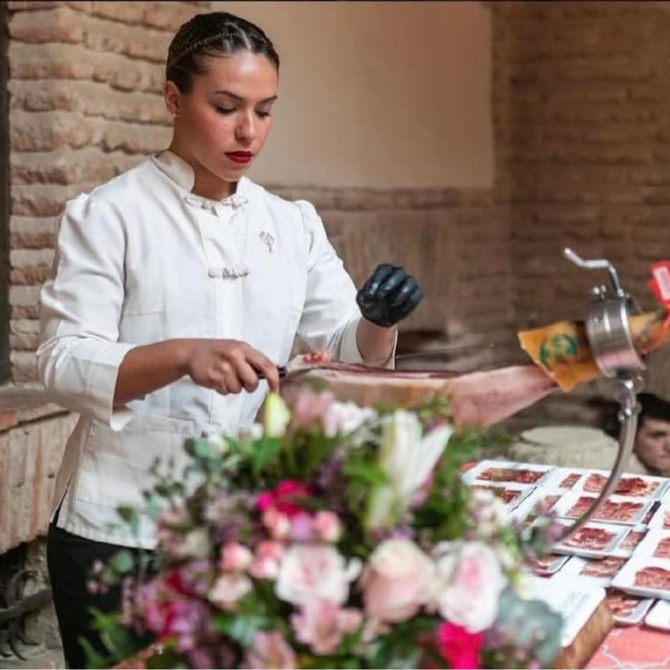 Neus Coronado corta jamón en un evento culinario.