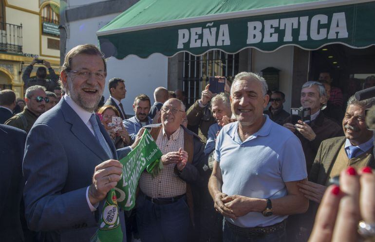 El jefe del Ejecutivo, Mariano Rajoy (i), es obsequiado con una bufanda del Real Betis en un peña futbolística en Tomares (Sevilla), donde hoy ha participado en una acto de precampaña del PP, en el que ha vuelto a criticar la inexperiencia de sus principales rivales en las urnas y se ha remitido a la época de Zapatero.