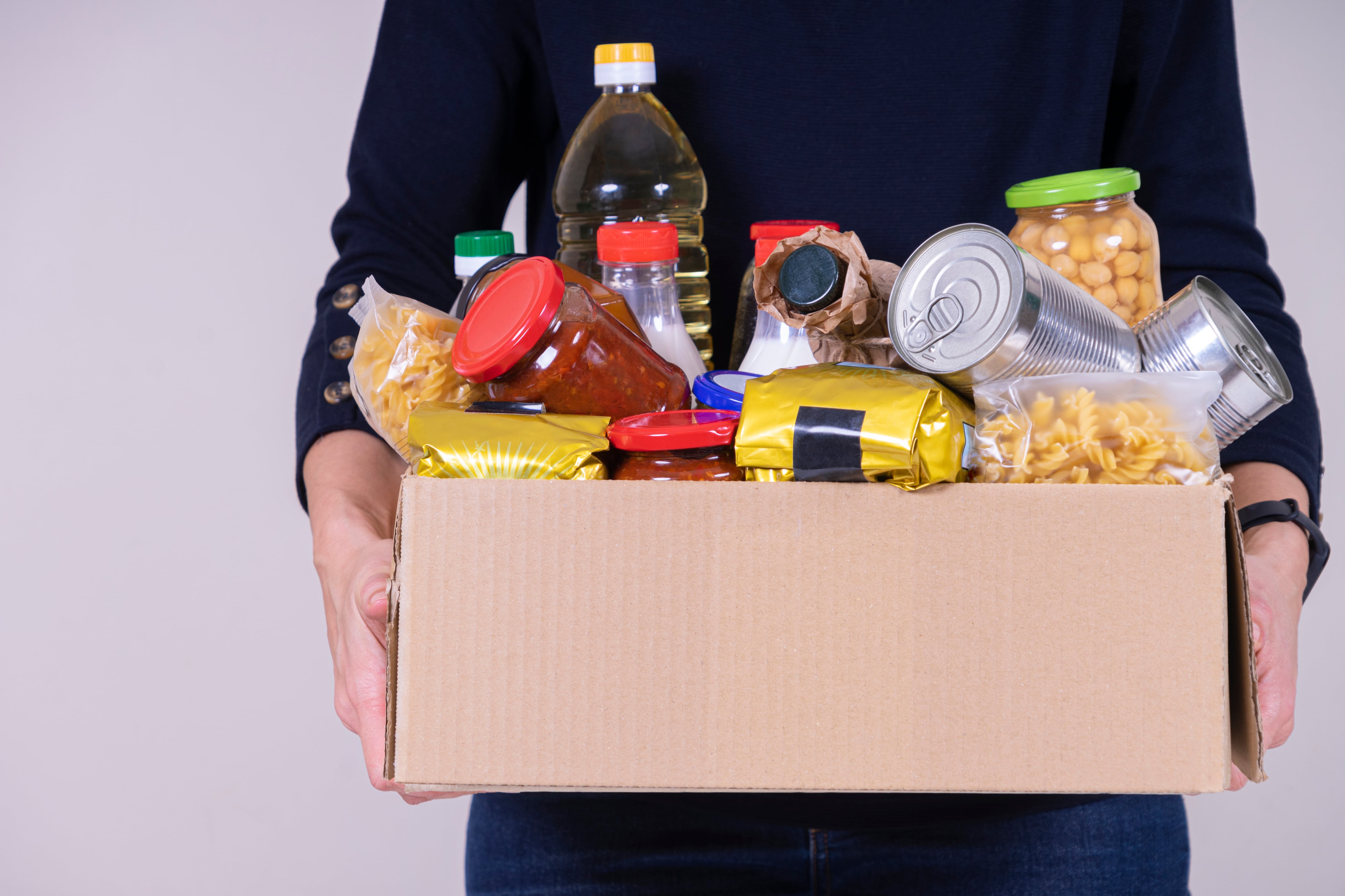 Woman volunteer hands holding food donations box with food grocery products.